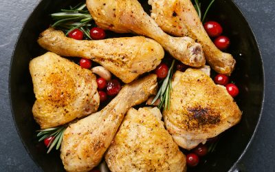 Tasty appetizing baked chicken legs served with spices, rosemary and cranberries on pan on stone background table. Christmas dish. View from above with copy space. Square